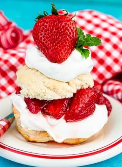 A serving of strawberry shortcake on a white plate with a blue background