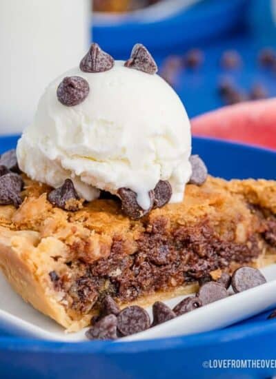 A close up photo of a piece of chocolate chip cookie pie topped with ice cream.