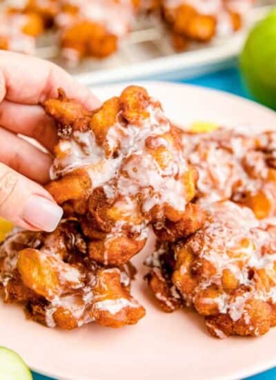 A hand grabbing an apple fritter from a plate.