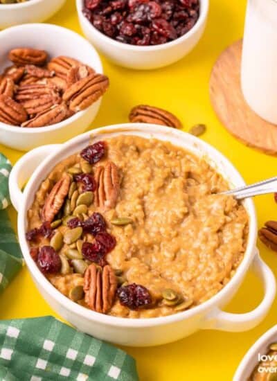 A bowl of pumpkin oatmeal topped with nuts, cranberries and seeds.