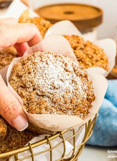 A hand grabbing a pumpkin streusel muffin from a basket.