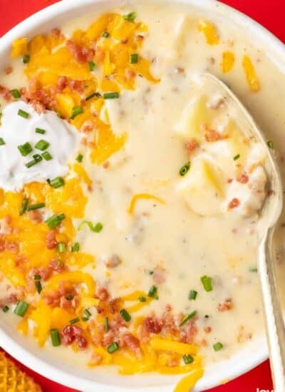 A bowl of sausage and potato soup topped with cheese, bacon and sour cream.