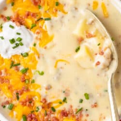 A bowl of sausage and potato soup topped with cheese, bacon and sour cream.