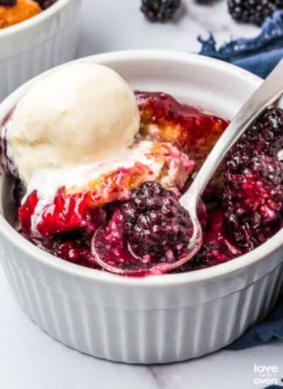 blackberry cobbler topped with ice cream in a ramekin with a spoon taking a bite out