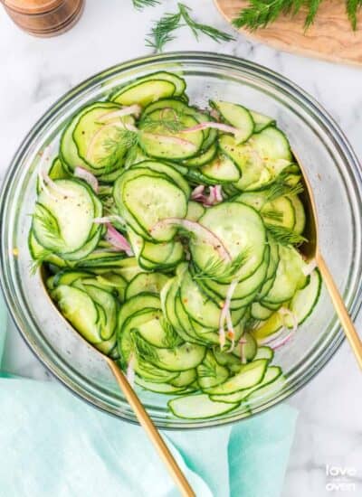 a serving bowl filled with cucumber salad with tongs in it