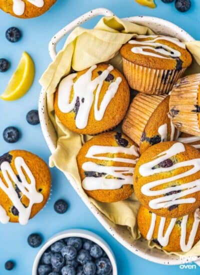 A bowl filled with lemon blueberry muffins with blueberries and lemon slices around it.