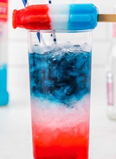 A bomb pop sitting on top of a glass of red white and blue cocktail