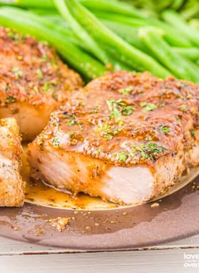 a honey mustard pork chop on a plate with green beans