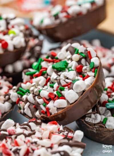 A variety of hot chocolate bomb cups laying together on a plate topped with Christmas sprinkles.