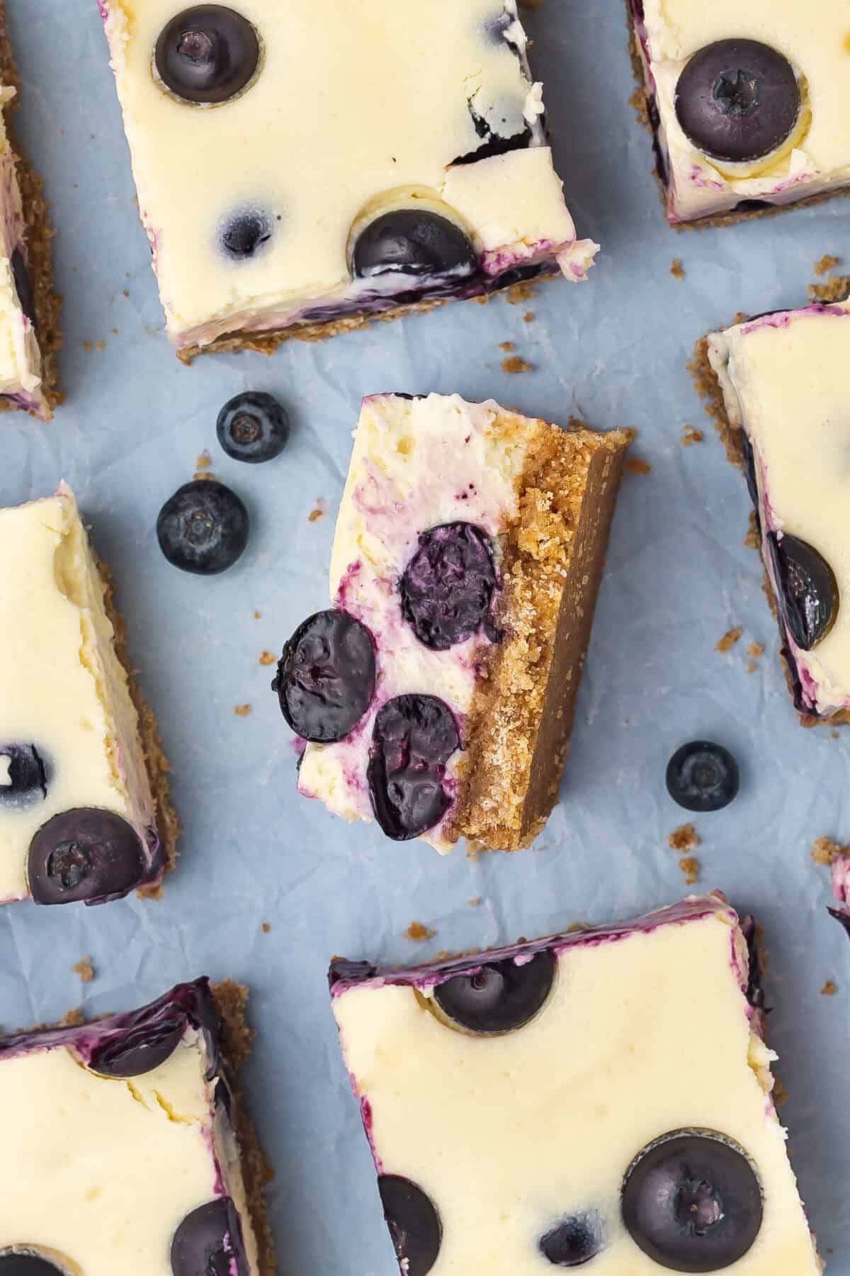 Blueberry cheesecake bars cut and on a blue background
