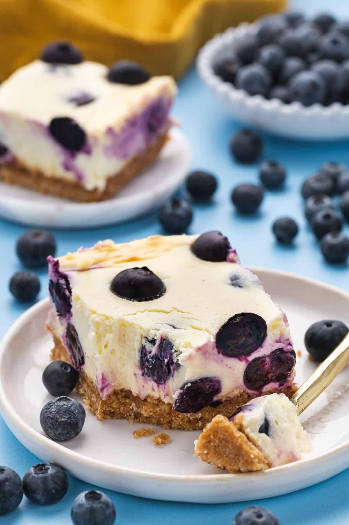 A slice of blueberry cheesecake on a plate with a fork.