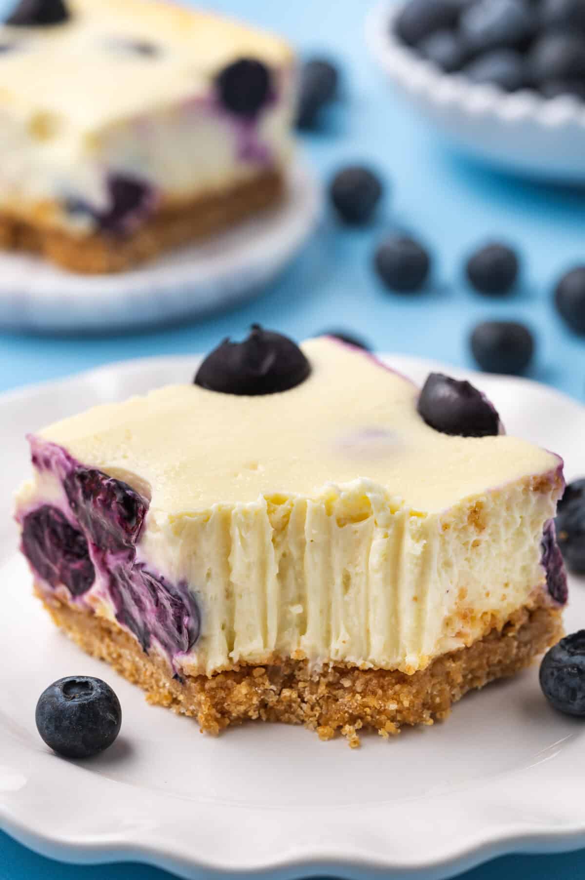 A blueberry cheesecake bar with a bite taken out of it sitting on a plate.