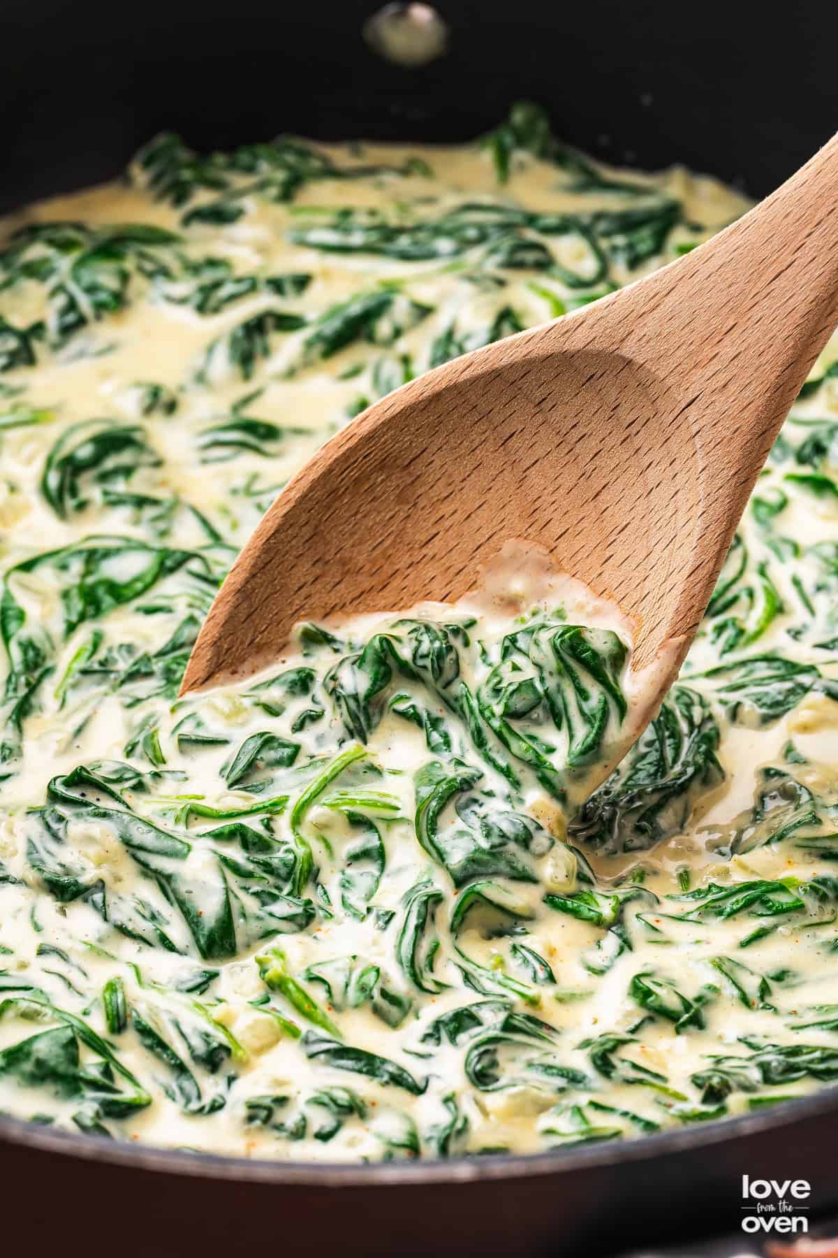 Creamed spinach in a pan with a wooden spoon