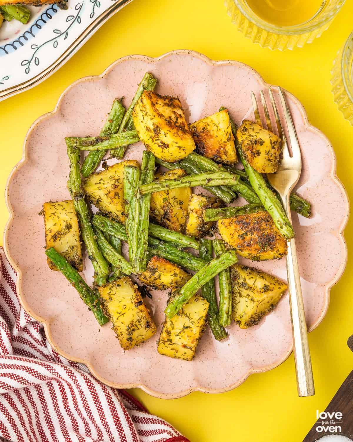 A pink plate with green beans and potatoes on it