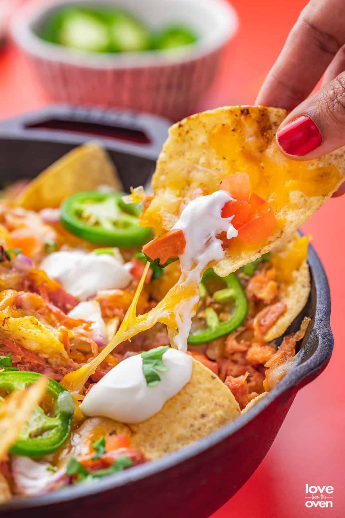 A hand grabbing a pulled pork nacho from a pan