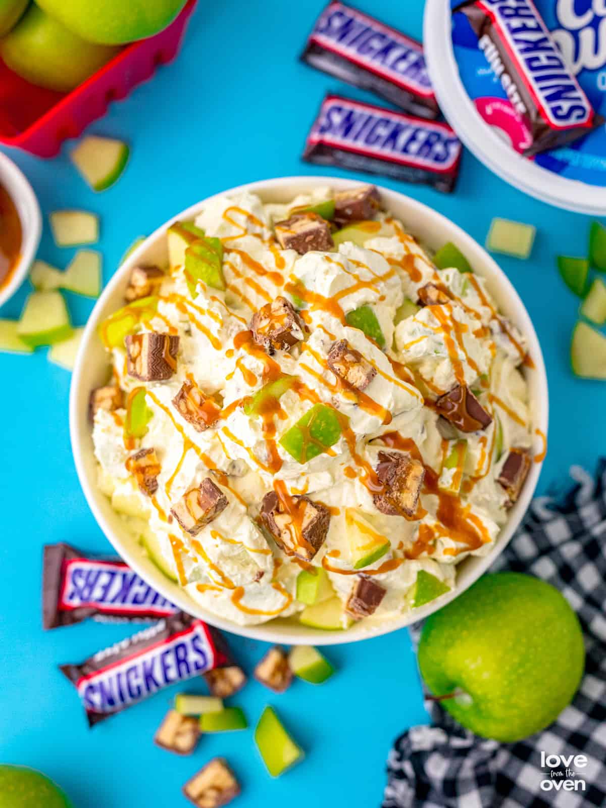 A bowl of snickers apple salad surrounded by bite size snickers bars