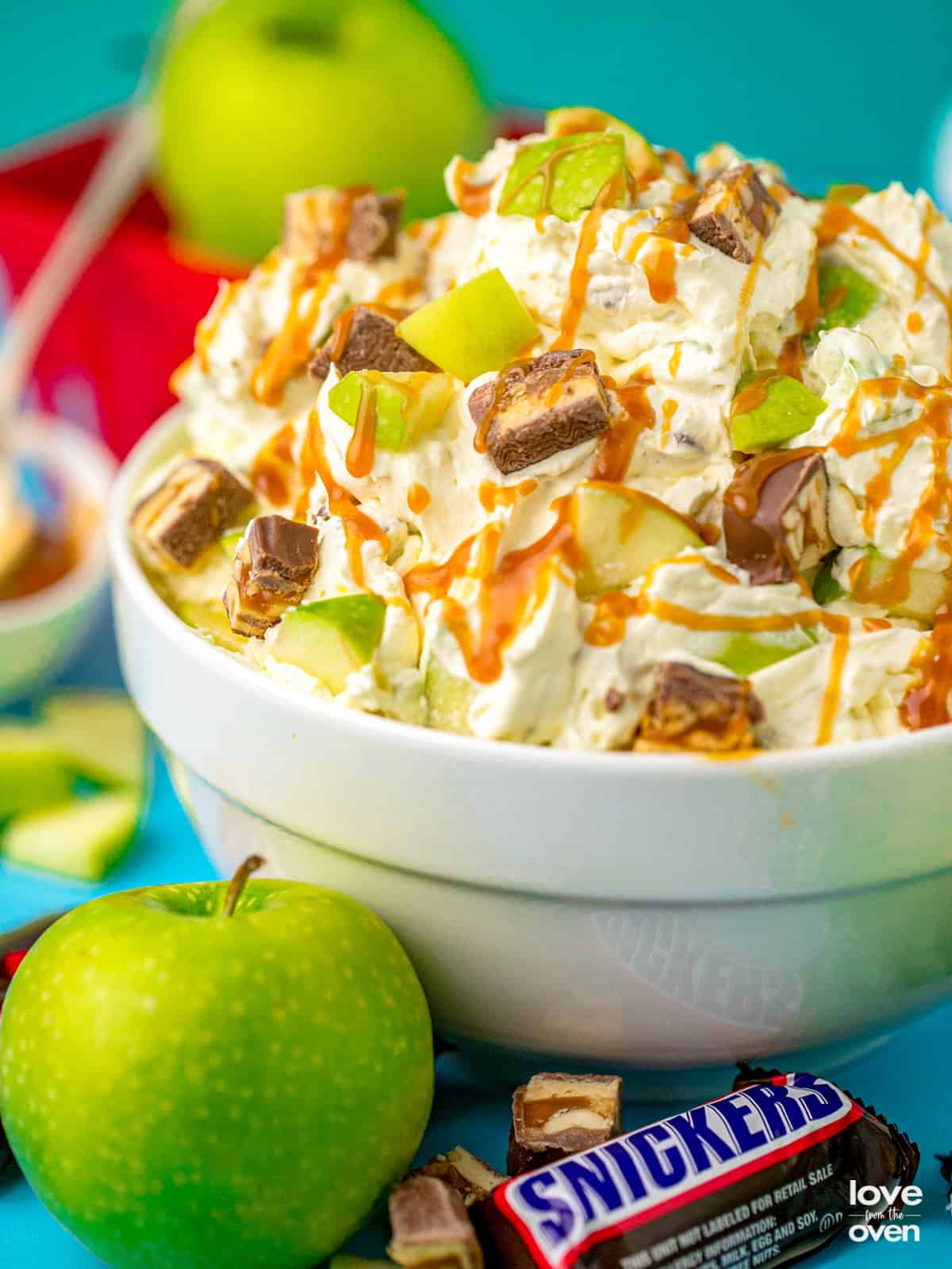 A bowl of snickers apple salad with an apple and a snickers bar.