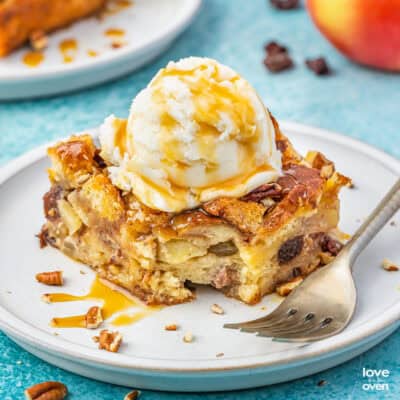 A slice of apple bread pudding on a white plate with a fork