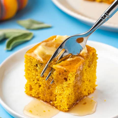 A fork cutting into a piece of pumpkin cornbread with butter on top