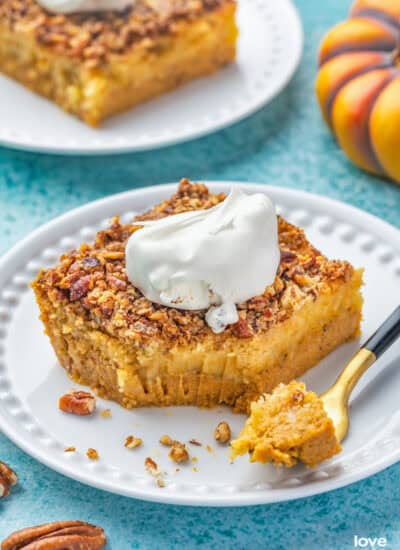 Slices of pumpkin crunch cake on white plates topped with whipped cream