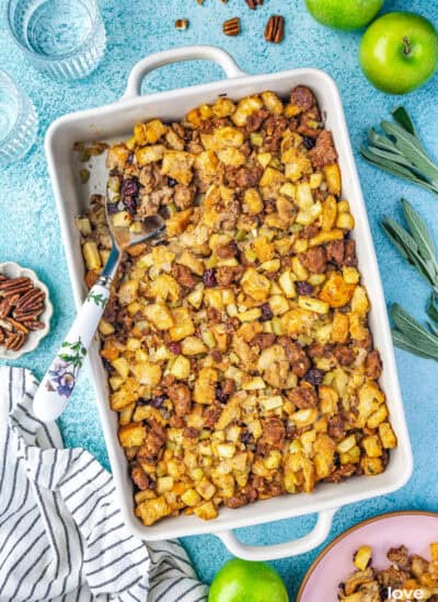 An overhead photo of a white casserole dish containing sausage apple stuffing and a spoon